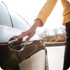 Hand reaches for a car door handle.